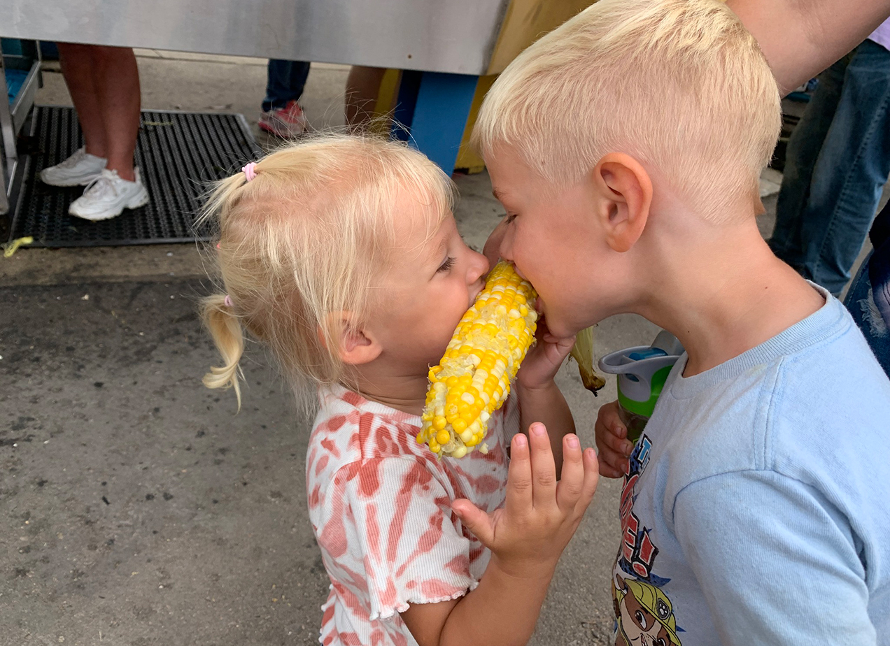 Kids eating corn on the cob at the fair.
